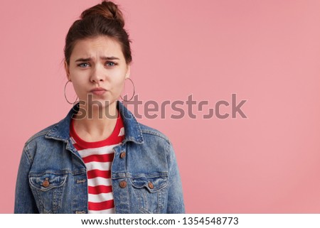 Unhappy cute young woman in denim jacket striped t-shirt , frowning her face and looking at camera, isolated over pink background. Female thinking about difficult situation in her life. Royalty-Free Stock Photo #1354548773