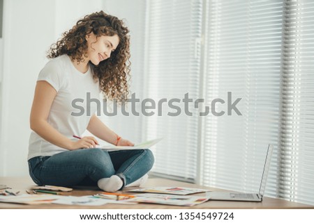 The happy woman sitting on the table and drawing on the paper