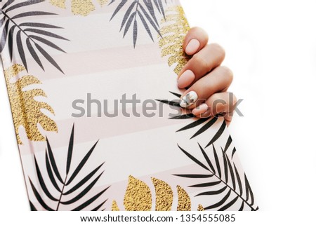 Woman's hands with unicorn perfect manicure holding notepad with leaves as mockup for your design. White background, flat lay style.