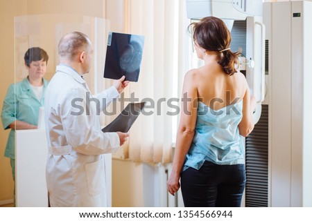 Male octor Standing Assisting Female Patient Undergoing Mammogram X-ray Tes. Man oncologist talking with her patient on mammography examination. Royalty-Free Stock Photo #1354566944