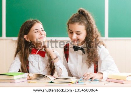 two beautiful schoolgirls are sitting at the desk with books in the classroom.