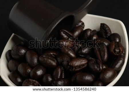Group of roasted robusta coffee beans on a small white bowl with a brown measuring spoon