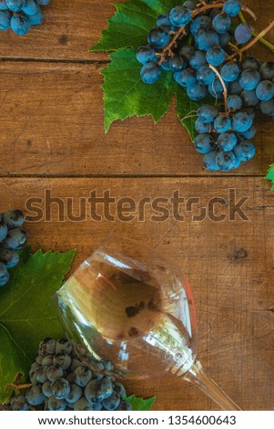 Black grapes with leaves and wineglasse with wine liying on the vintage wooden background with copy space. Vertical picture