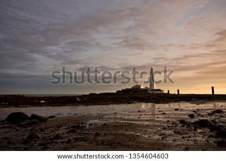 Sunrise over the North Sea in North East England. The sky is beginning to brighten up and is reflected in the calm waters. St Mary's Island and Lighthouse are on the horizon.