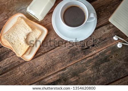 Flat lay picture of morning breakfast set which comprises of bread, bottle of milk and black hot coffee. Chilling out at home concept. The wood background has blank copy space to add notes or text. 