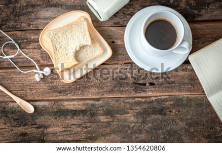 Flat lay picture of morning breakfast set which comprises of bread, bottle of milk and black hot coffee. Chilling out at home concept. The wood background has blank copy space to add notes or text. 
