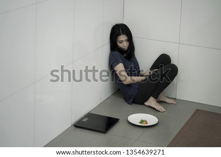 Picture of a skinny anorexic woman sitting with a plate of salad and weight scales in the bathroom. Weight loss concept