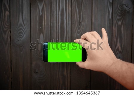 hand holding black cellphone with green screen isolated on wooden background