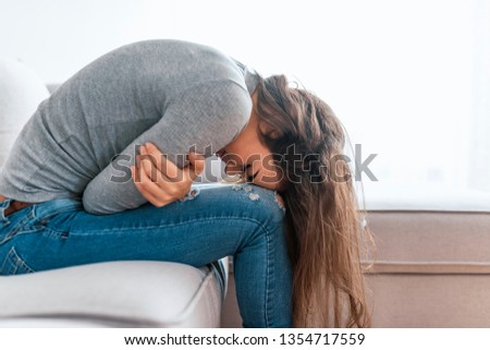 Young woman sitting on the bed with hard stomach pain. Healthcare medical or daily life concept : Close up stomach of young lady have a stomachache or menstruation pain sitting on a sofa..