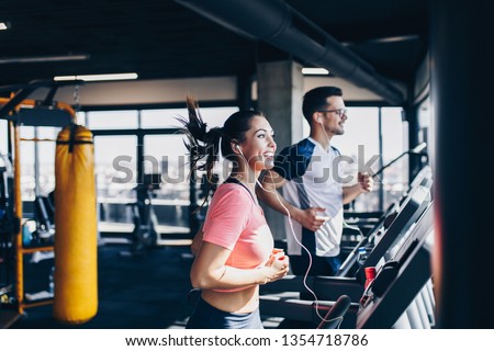 Young fit man and woman running on treadmill in modern fitness gym. Royalty-Free Stock Photo #1354718786