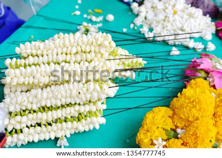 Preparation for make Thai traditional garland for make a merit in Songkran festival, pile of long needles with jasmine, pile of blurry marigold flowers in foreground, pure floral for Buddhist concept