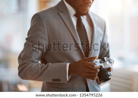 Young elegant businessman in formalwear looking at photocamera in his hands while going to take photos of something