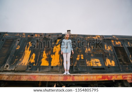 Portrait of a young woman against the background of the thrown rusty railway car