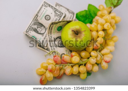 Green and yellow grapes and dollars. The cost of grapes. Expensive or cheap fruit. An Apple. Fruit cost