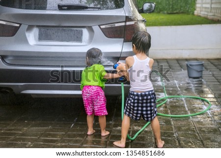 Picture of two little kids washing a car by using a water hose and sponge at home