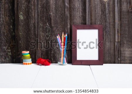 brown painted picture frame, pencils, white table, old wooden wall