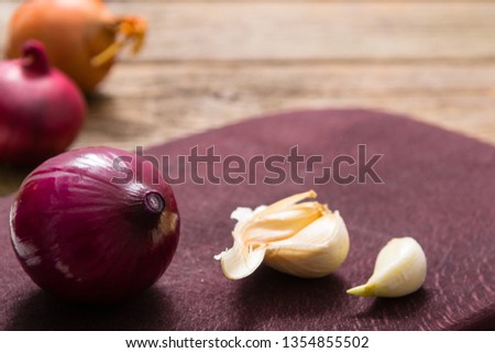 onions and garlics on cutting board, weathered wooden background