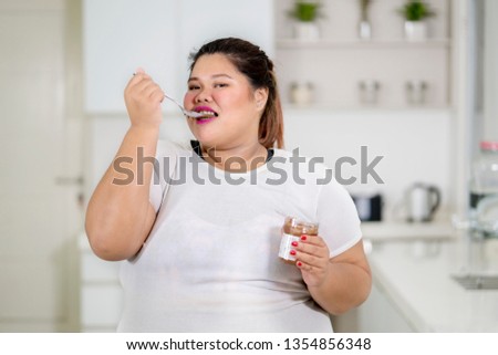 Picture of overweight woman enjoys chocolate cream with a spoon at home