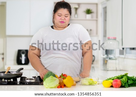 Picture of overweight woman chopping vegetables while preparing meals in the kitchen