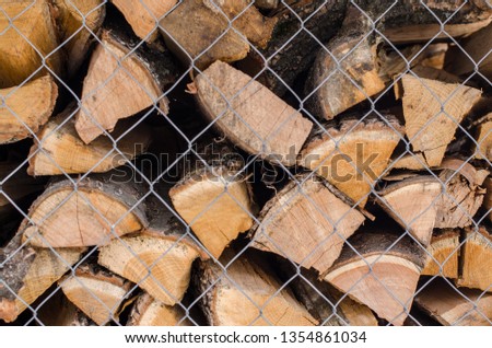 Wood pile reserve for the winter concept. Pile of chopped firewood from trees. Nature background texture of wood.  Wooden logs wall close up view behing the grid.
