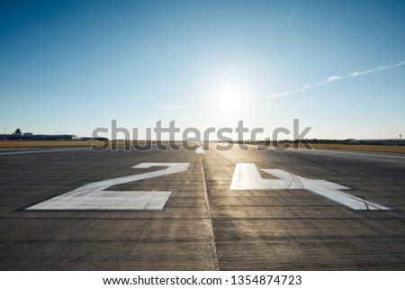 Surface level of airport runway with road marking and number 24 against clear sky. Royalty-Free Stock Photo #1354874723