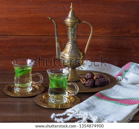 Conceptual picture of Ramadan food: dates, mint tea with mint leaves in a small tea cups with an old tea pot. Iftar or Suhoor snack close up with rustic background 