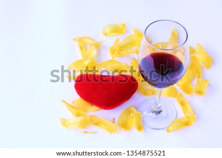 Close-up - red heart lies on the yellow tulip petals, a glass of red wine stands nearby.
