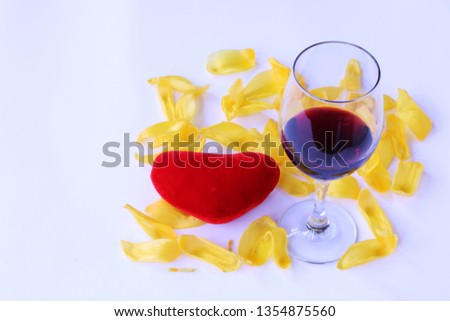 Close-up - red heart lies on the yellow tulip petals, a glass of red wine stands nearby.