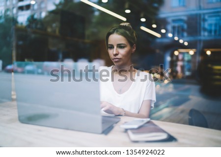 Serious woman concentrated on online webinar about languages for programming on laptop device, caucasian female copywriter working remote on freelance in cozy coffee shop interior via modern netbook