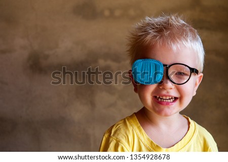 Portrait of funny child in new glasses with patch for correcting squint 
Ortopad Boys Eye Patches nozzle for glasses for treatment of strabismus (lazy eye) Royalty-Free Stock Photo #1354928678