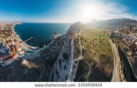 Genoese fortress in Sudak, Crimea. Aerial panorama view of ruins of ancient historic castle on crest of mountain near sea and small town at foot of rocks. Beautiful summer tourist landscape
