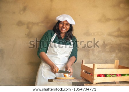 Attractive Indian woman cook cuts vegetables by knife. Closeup portrait of young beautiful woman. Positive emotions, facial expressions, feelings, signs and symbols, body language. white chef uniform