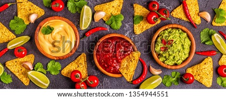 Mexican food background: guacamole, salsa, cheesy sauces with ingredients on black background, top view.