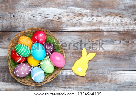 Colorful easter eggs in basket with gypsophila flowers and gingerbread cookie on wooden table