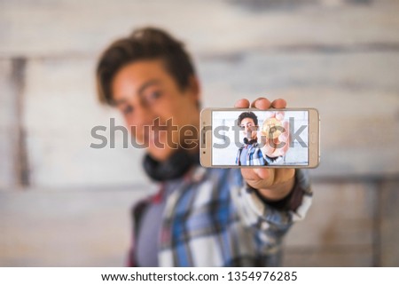 teenager with big smile and headphones showing pn the phone screen his photo with a bitcoin in his hand - modern money and youth modern people with technology - cripto currency concept