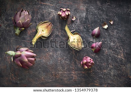 Flat lay with fresh red artishokes, while and halved, on dark background Royalty-Free Stock Photo #1354979378