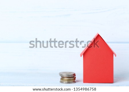 Red paper house with coins on wooden table
