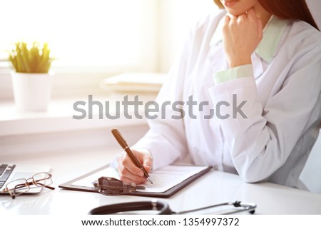 Doctor woman working with medication history records form while sitting at the desk near window in hospital. Medicine and health care concept. Green is main color