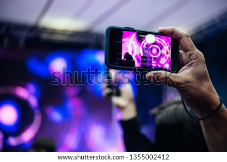 A person taking photo or video with his smartphone during a concert or a performance.