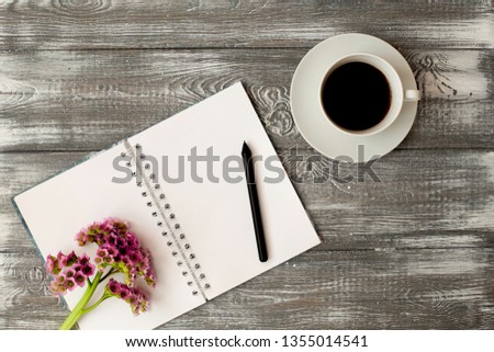 Blank diary or notebook with a spring, a pencil and a cup of coffee and pink flower on a gray shabby wooden table. Flat design.