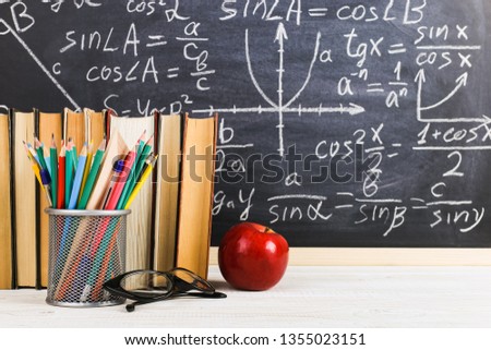 School desk in the classroom, with books on background of chalk board with written formulas. Soncept Teacher's Day.