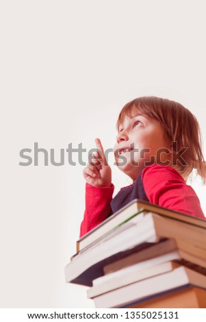 Little cute child girl pointing with finger up on the stack of books as symbol of education, studies and self development.