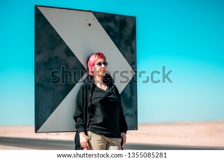 A woman stands near a road sign in the desert and waits for a car. Hitch-hiking.