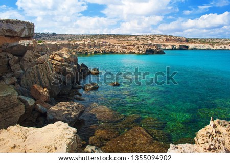 Image of Blue Lagoon bay near Cape Greco, Cyprus. View of rock coastline near deep green transparent emerald water against a rocky hill. Amazing cloudscape. Warm day in fall