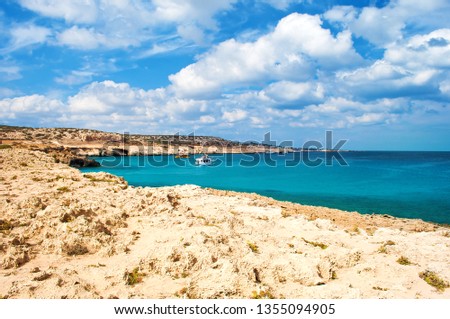View of the Blue Lagoon bay near Cape Greco, Cyprus. Rock coastline near deep green transparent azure water, one white boat. Amazing cloudscape. Warm day in fall