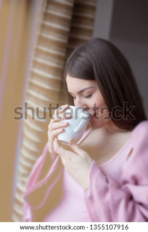 Portrait of beautiful pregnant woman smelling coffee,standing next to window.