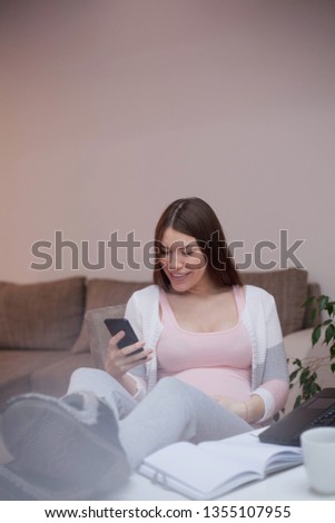 Pregnant smiling woman in home office using smart phone.