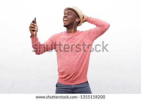 Portrait of happy young african american man listening to music with smart phone and earphones against white background