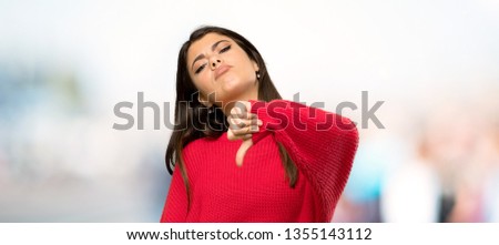 Teenager girl with red sweater showing thumb down with negative expression at outdoors