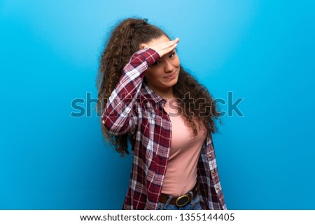 Teenager girl over blue wall looking far away with hand to look something